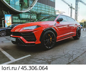 Красный автомобиль Lamborghini Urus припаркован перед современным офисным зданием. Блестящий итальянский внедорожник на улице. Редакционное фото, фотограф Константин Григорьев / Фотобанк Лори