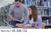Young positive interested couple of students spending time together in library, reading books and browsing educational websites on laptop. Стоковое видео, видеограф Яков Филимонов / Фотобанк Лори