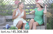 European young woman in straw hat is sitting on wooden bench and chatting sweetly with her sister. Стоковое видео, видеограф Яков Филимонов / Фотобанк Лори