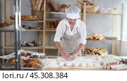 Skilled female baker in striped apron carefully handling individual dough portions at flour-covered worktable, surrounded by freshly baked bread, ingredients and tools in artisan bakery. Стоковое видео, видеограф Яков Филимонов / Фотобанк Лори