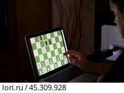 A man solves a chess problem online. Chess board with figures on a laptop screen. Leisure in self-isolation, in the twilight. International chess day. Стоковое фото, фотограф Vadzim Yakubovich / Фотобанк Лори