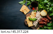 Плоская деревенская говядина с белой фасолью, колбасой, крекерами и свежим базиликом. Стоковое AI-изображение, AI-художник ФотоИнтеллект / Фотобанк Лори