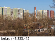 Вид на многоэтажные панельные жилые дома. На переднем плане деревья и промышленная труба. Жилые кварталы в спальном районе большого города. Городские окраины. Стоковое фото, фотограф Андрей Степанов / Фотобанк Лори