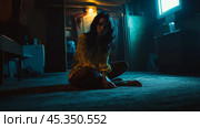 A woman sitting alone on a carpeted floor in a dimly lit room with a television glowing in the background during nighttime. Стоковое AI-изображение, AI-художник Сергей Толмачёв / Фотобанк Лори