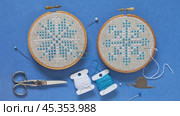Video of two hand embroidered cross stitch snowflakes in hoops on blue background and accessories for cross stitch. Winter crafts and Christmas gifts concept. Cross stitches as hobby. Flat lay, close-up. Стоковое видео, видеограф Виктория Катьянова / Фотобанк Лори
