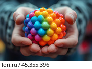 Яркая разноцветная игрушка в ладонях. Стоковое AI-изображение, AI-художник Щеголева Ольга / Фотобанк Лори