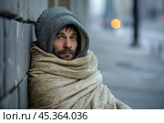 Houseless person wrapped in an old blanket sitting on a city street. concept of deprivation, vagrancy, homelessness. Стоковое AI-изображение, AI-художник 123 12 / Фотобанк Лори