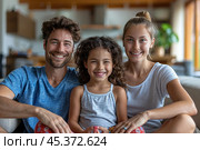 Loving young man hug his beloved wife and little daughter sit on couch in living room, happy people smiling looking at camera posing for photo picture. Exemplary family portrait, love and bond concept. Стоковое AI-изображение, AI-художник Ирина Михайличенко / Фотобанк Лори