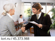 Smiling businessman with papers shaking hands with elderly woman. Стоковое фото, фотограф Яков Филимонов / Фотобанк Лори