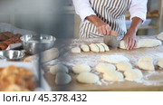 Close-up of skilled baker hands cutting soft dough with scraper on floured wooden worktable, filled with baking tools and ingredients, in bakery. Стоковое видео, видеограф Яков Филимонов / Фотобанк Лори