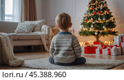 Christmas at home. Waiting for miracles and a gift. A cute little boy is sitting on the floor in a bright living room decorated for Christmas and New Year holidays. Стоковое AI-изображение, AI-художник Photojuli / Фотобанк Лори