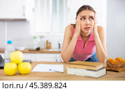Young woman with headache standing near table with books at home. Стоковое фото, фотограф Татьяна Яцевич / Фотобанк Лори
