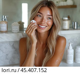 A blonde woman with a radiant smile stands in front of a mirror in a bright bathroom. She applies face cream, her skin looks fresh and smooth. Created by AI. Стоковое AI-изображение, AI-художник Ярославский Максим / Фотобанк Лори