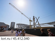 Строительство нового железнодорожного вокзала в городе Грозный, Чеченская Республика, Россия. Вид на строительные краны и высокую башню строящегося вокзала. Мимо строительной площадки идут пассажиры. Реконструкция железнодорожной станции и возведение современного вокзального комплекса в Чечне. Развитие транспортной инфраструктуры на Северном Кавказе. (2024 год). Редакционное фото, фотограф Андрей Степанов / Фотобанк Лори