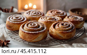 The cinnabons. Close-up of cinnamon buns. Beautiful buns with fresh cinnamon and icing on a wooden table. Fragrant homemade New Year's pastries. Стоковое AI-изображение, AI-художник Photojuli / Фотобанк Лори