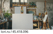 Blank canvas stands on easel in sunny art studio, brushes, paints and artwork surround it. Стоковое AI-видео, аниматор Юрий Поздников / Фотобанк Лори
