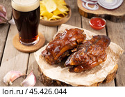 Deliciously cooked pork hooves with a side of crispy chips and a dark drink on a rustic wooden table. Стоковое фото, фотограф Евгения Трушкова / Фотобанк Лори