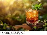 Mint Julep cocktail with ice and fresh mint sprig in a crystal glass. Evening scene with blurred greenery and warm sunlight bokeh in the background. Стоковое AI-изображение, AI-художник Башкирова Анна / Фотобанк Лори