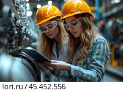 A photo of two young female engineers working in an industrial setting. They are in a factory or manufacturing facility, both wearing orange safety helmets and clear safety glasses, highlighting the importance of safety in the workplace. The women are focused on a tablet, analyzing or checking equipment. The background is blurred, with elements of large industrial equipment, creating an atmosphere of modern technology and high-precision manufacturing. The photo would be great for illustrating themes of engineering, manufacturing, technology, and also for demonstrating gender equality in technical professions. Стоковое AI-изображение, AI-художник Анна Кривицкая / Фотобанк Лори