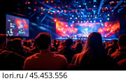 Spectators are seated in a large arena, their backs to the camera, focused on a brightly lit stage. Стоковое AI-изображение, AI-художник Сергей Толмачёв / Фотобанк Лори