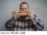 Fat man eats a huge meat sandwich with gusto. Стоковое AI-изображение, AI-художник Дмитрий Киселёв / Фотобанк Лори