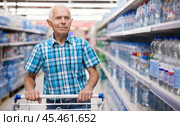 elderly retired man buying bottle of drinking water in alcohol section of supermarket. Стоковое фото, фотограф Татьяна Яцевич / Фотобанк Лори