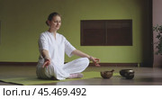 A woman practices kundalini yoga sitting in a lotus position on a mat in a room, performs various mudras connecting her fingers alternately, trains in white loose clothes. Стоковое видео, видеограф Сергей Чайко / Фотобанк Лори