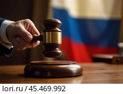 A hand with a wooden judge's hammer on the background of the tricolor Russian flag. Стоковое AI-изображение, AI-художник RamA / Фотобанк Лори