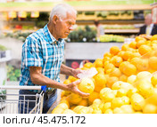Mature senor examines oranges in fruit section of supermarket. Стоковое фото, фотограф Татьяна Яцевич / Фотобанк Лори
