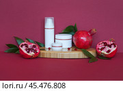 Natural cosmetic moisturizers for face and hands: cream, mousse, lotion with vitamin extract of pomegranate on wooden podium and burgundy background. Use of vitamin fruit extracts in cosmetics. Стоковое фото, фотограф Виктория Катьянова / Фотобанк Лори