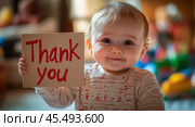 A one-year-old infant sits on a comfy bed, holding a cardboard sign reading "Thank you." Стоковое AI-изображение, AI-художник Ярославский Максим / Фотобанк Лори