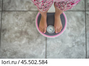 A woman stands on a scale in a brightly lit bathroom, feeling disheartened as she peers down at the numbers, revealing her emotions about her weight. Стоковое AI-изображение, AI-художник Sergey Grishin / Фотобанк Лори