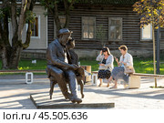 Памятник писателю Александру Ивановичу Куприну, город Гатчина, Ленинградская область, Россия. Скульптурный портрет мужчины, сидящего в кресле и читающего газету. На скамейке сидят женщины и смотрят в смартфоны. Сопоставление традиционных и современных способов получения информации. Памятник установлен в городском сквере Гатчинский дворик в историческом центре Гатчины. Туристическая достопримечательность. Редакционное фото, фотограф Андрей Степанов / Фотобанк Лори