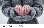 Women's hands in warm mittens hold a pink heart. Snow is falling. Valentine's Day and World Health, Love and Family Insurance Day. Стоковое AI-изображение, AI-художник Photojuli / Фотобанк Лори