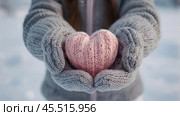Women's hands in warm mittens hold a pink heart. Snow is falling. Valentine's Day and World Health, Love and Family Insurance Day. Стоковое AI-изображение, AI-художник Photojuli / Фотобанк Лори