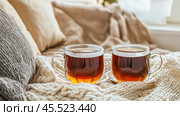 Two glass cups of hot tea resting on cozy grey knitted blanket. Стоковое AI-изображение, AI-художник Юрий Поздников / Фотобанк Лори
