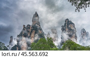 Amazing unusual mountains. Steep high cliffs with green vegetation on the slopes are surrounded by fog. Peaks against the background of clouds and sky. China. The landscape of the Golden Whip Brook. Стоковое фото, фотограф Вера Ивановна Кубарева / Фотобанк Лори