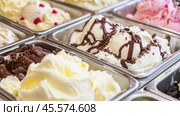 Chocolate, vanilla, strawberry ice cream tubs. Freshly churned various ice cream in a metal containers. Freezer full of icecream in the boxes in cooled counter. Gelato display of many flavors. Стоковое AI-изображение, AI-художник Марина Демидюк / Фотобанк Лори