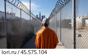 Man walks toward downtown skyline through a fenced pathway under clear blue skies in Los Angeles. Стоковое AI-изображение, AI-художник Сергей Толмачёв / Фотобанк Лори