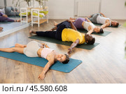 Young woman coach and students perform Supta Ardha Matsyendrasana during training in studio. Стоковое фото, фотограф Яков Филимонов / Фотобанк Лори