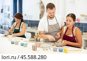 Pupils are sitting near work table, sculpting plate of raw clay under supervision of male teacher. Стоковое фото, фотограф Яков Филимонов / Фотобанк Лори