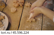 Female hands of pastry chef, using pastry bag, squeeze out white glaze to create pattern on ginger cookie shaped like man. Стоковое видео, видеограф Strunov David / Фотобанк Лори