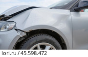 Front view of silver car with damaged hood and fender. Scratches and dents from accident. Focus on headlight, wheel, tire. Impact damage needs repair. Стоковое фото, фотограф Павел Муравьев / Фотобанк Лори