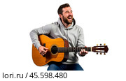 Happy guy in gray hoodie sitting and playing acoustic guitar, isolated on white background, casual style, enjoying music, musician strumming strings, relaxed mood. Стоковое AI-изображение, AI-художник Павел Муравьев / Фотобанк Лори