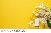 A glass bottle filled with homeopathic globules is placed on a bright yellow background, surrounded by white flowers, showcasing alternative medicine in a vibrant setting. Стоковое AI-изображение, AI-художник Sergey Grishin / Фотобанк Лори