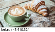 Green ceramic cup of frothy cappuccino coffee with croissants on rustic wood background. Hot latte with art milk foam and freshly-baked Brioche on cafe table. Breakfast or coffee break. Morning ritual. Стоковое AI-изображение, AI-художник Марина Демидюк / Фотобанк Лори