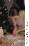 A young female baker is preparing ginger cookies, using red icing to decorate them. Стоковое видео, видеограф Strunov David / Фотобанк Лори