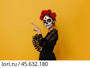Оранжевый фон с девушкой в наряде дня мертвых указывает пальцем. Стоковое AI-изображение, AI-художник Александр Жуков / Фотобанк Лори