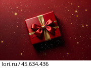 Perfect red Christmas present gift box with elegant gold bow ribbon on red background near stars. Greeting gift symbolize lovely holiday gifting. Birthday Christmas festive concept. Copy ad text space. Стоковое AI-изображение, AI-художник Aleksandr Golubev / Фотобанк Лори