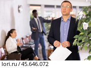 Upset middle-aged man standing in waiting room with his back to person who is shouting at him. Стоковое фото, фотограф Яков Филимонов / Фотобанк Лори